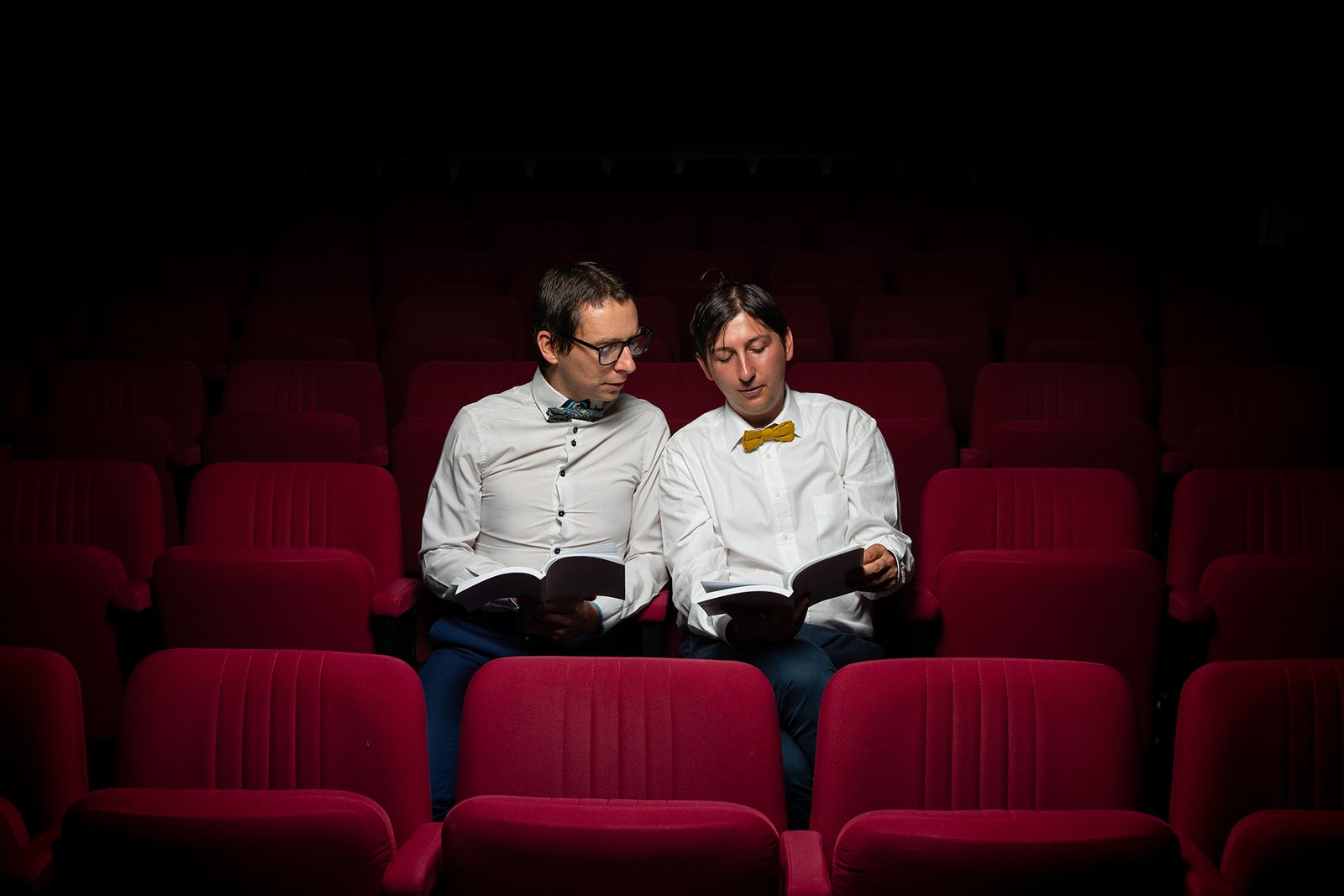 Deux comédiens du spectacle Hautes Définitions lisent un texte dans une salle de théâtre à Bordeaux, assis parmi les fauteuils rouges.