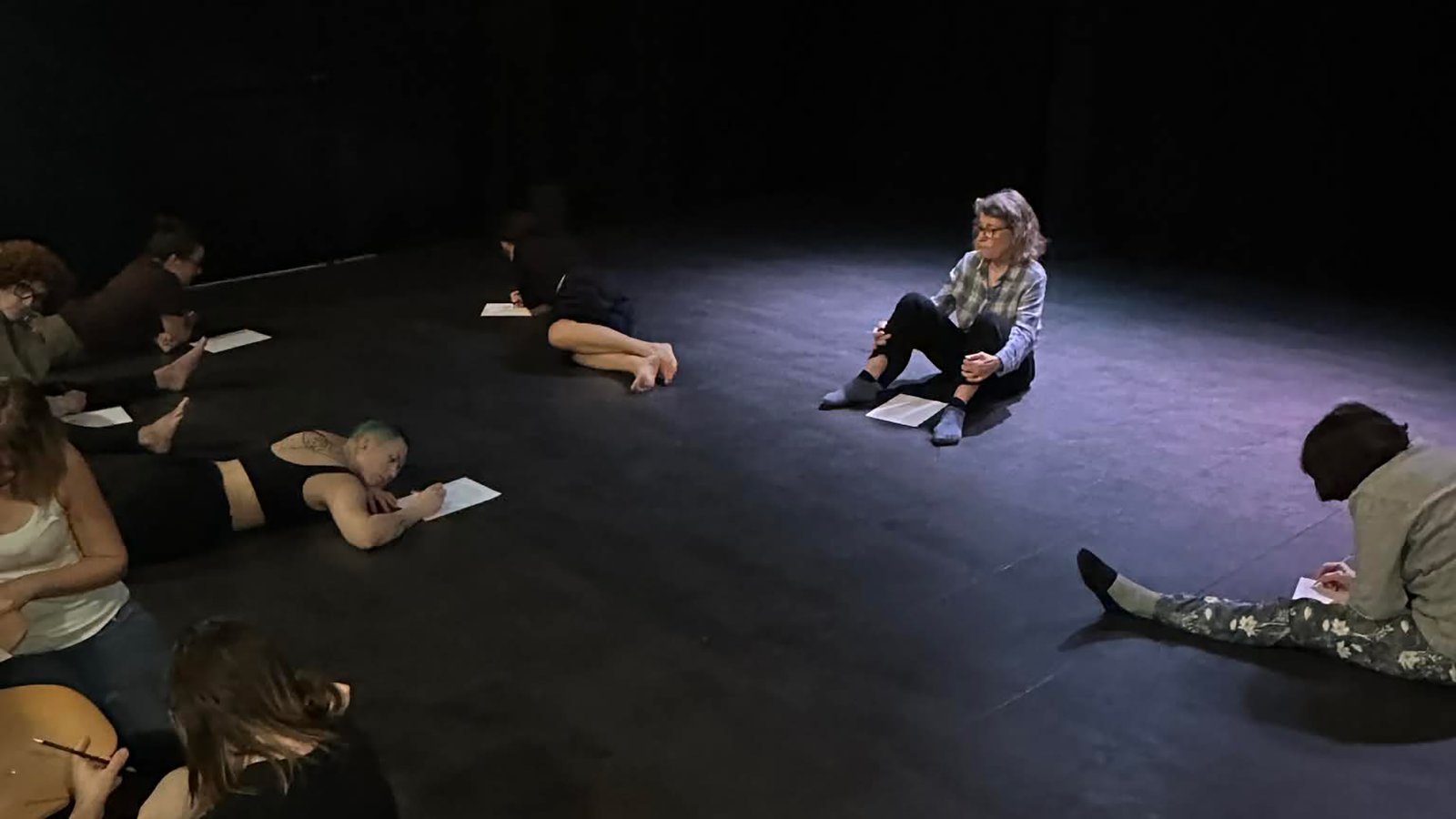 Participants d’un stage de théâtre à Bordeaux assis sur scène en train d’écrire et de réfléchir lors d’un exercice d’expression.