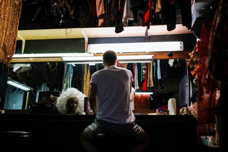 An anonymous person preparing backstage with costumes, wigs, and mirrors in a dressing room.